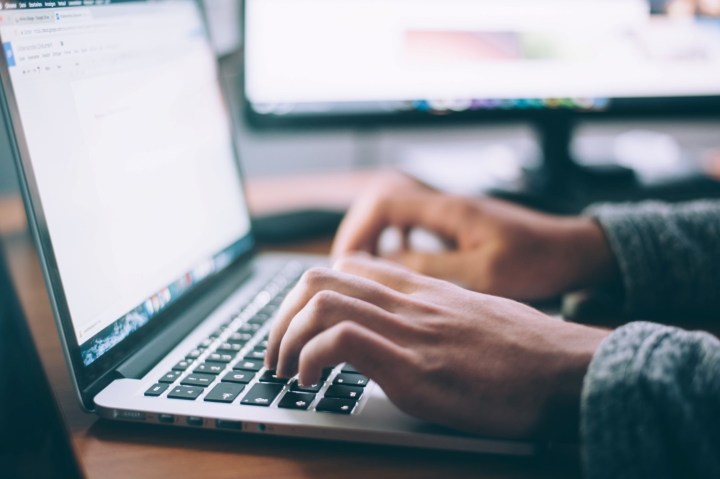 A closed up picture of a person's hands showing them working on a laptop.